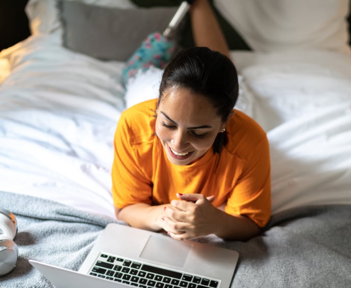 Femme en haut orange allongée sur son lit.